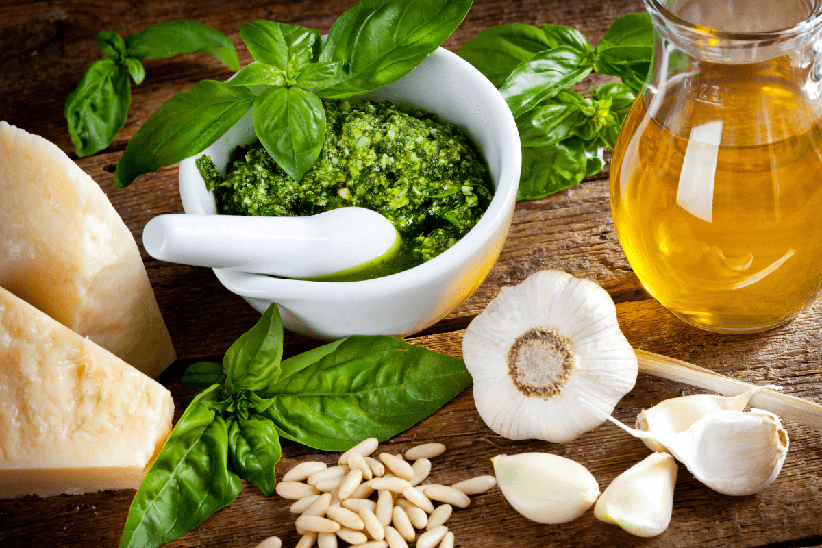 Frische Zutaten für Pesto: Basilikum, Pinienkerne, Knoblauch, Parmesan und Olivenöl in Schalen und auf Holzuntergrund.