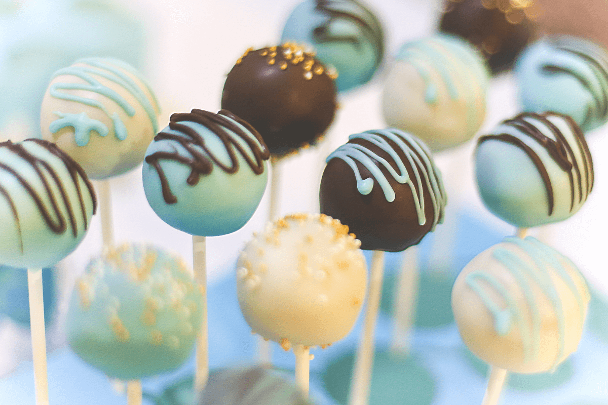 Bunte Cake-Pops in verschiedenen Farben, dekoriert mit Schokolade und Streuseln, auf weißen Stielen präsentiert.
