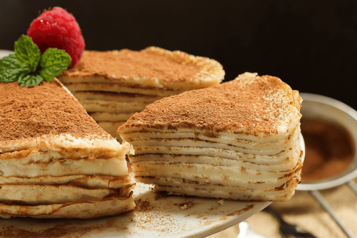 Schichttorte mit dünnen Crepes und einer Füllung aus Sahne, bestäubt mit Kakaopulver, garniert mit Himbeere und Minze.