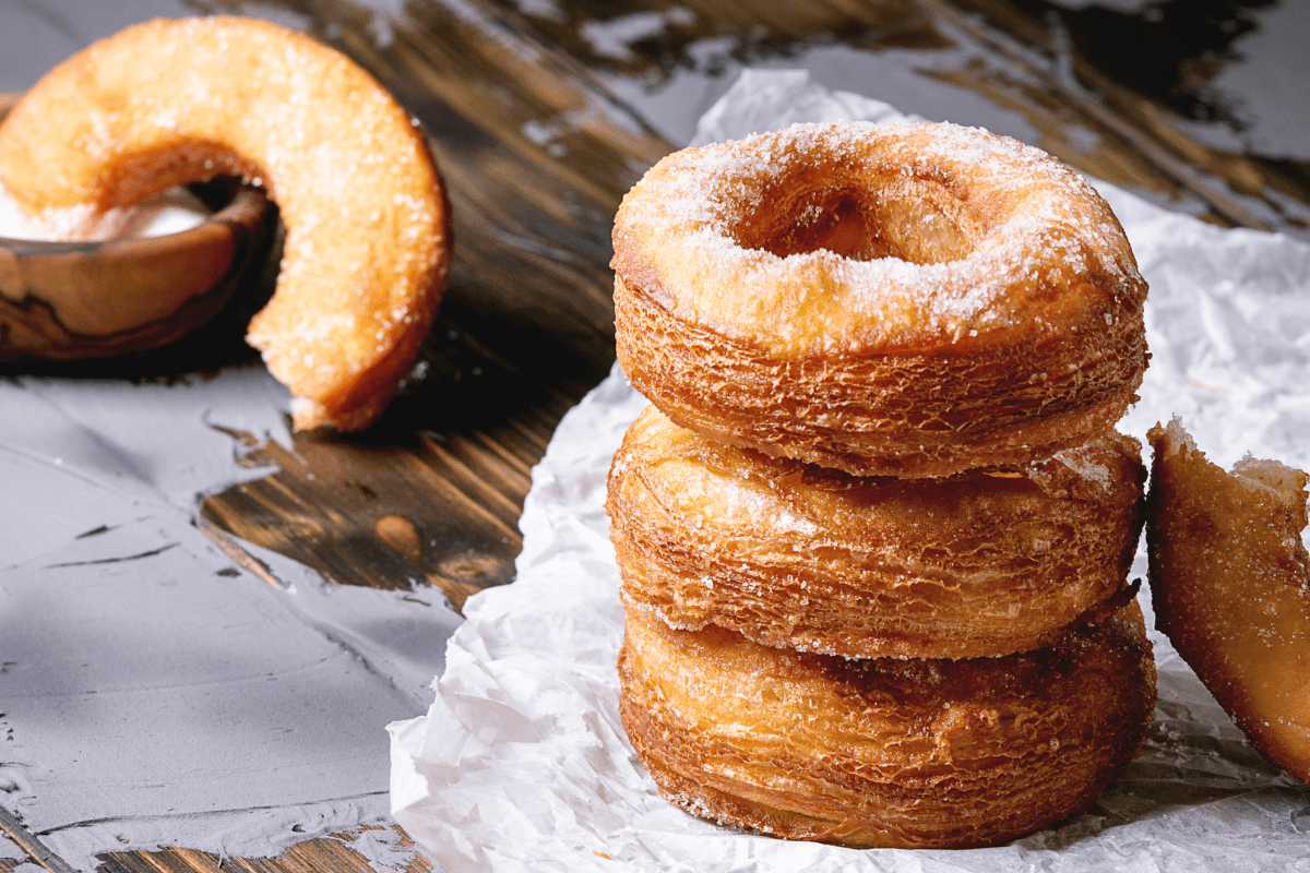 Drei übereinander gestapelte Cronuts mit Zucker bestreut, daneben ein halber Cronut auf einer Serviette.