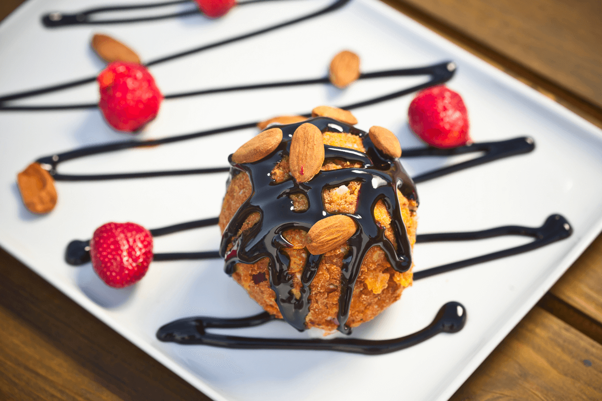 Frittiertes Eis mit Schokoladensoße, garniert mit Mandeln und frischen Erdbeeren auf einem weißen Teller.