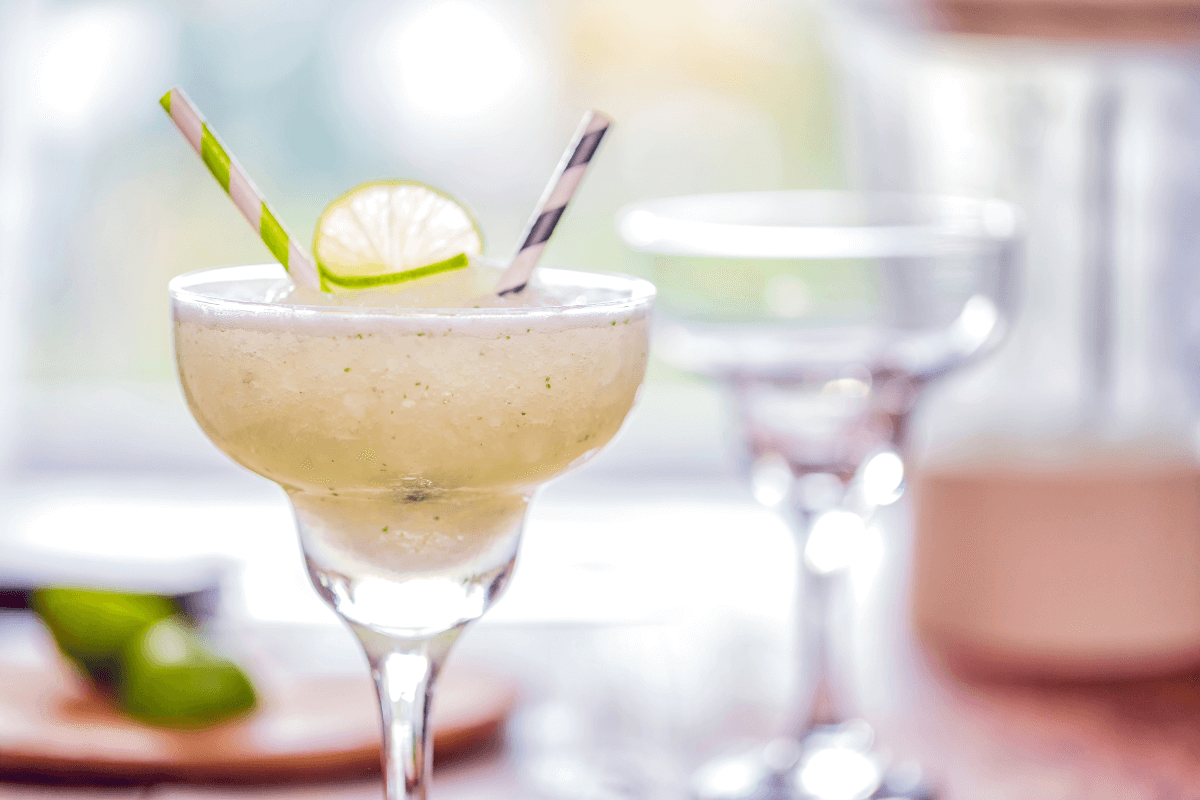 Gefrorene Margarita in einem eleganten Glas, garniert mit Limettenscheibe und bunten Strohhalmen.