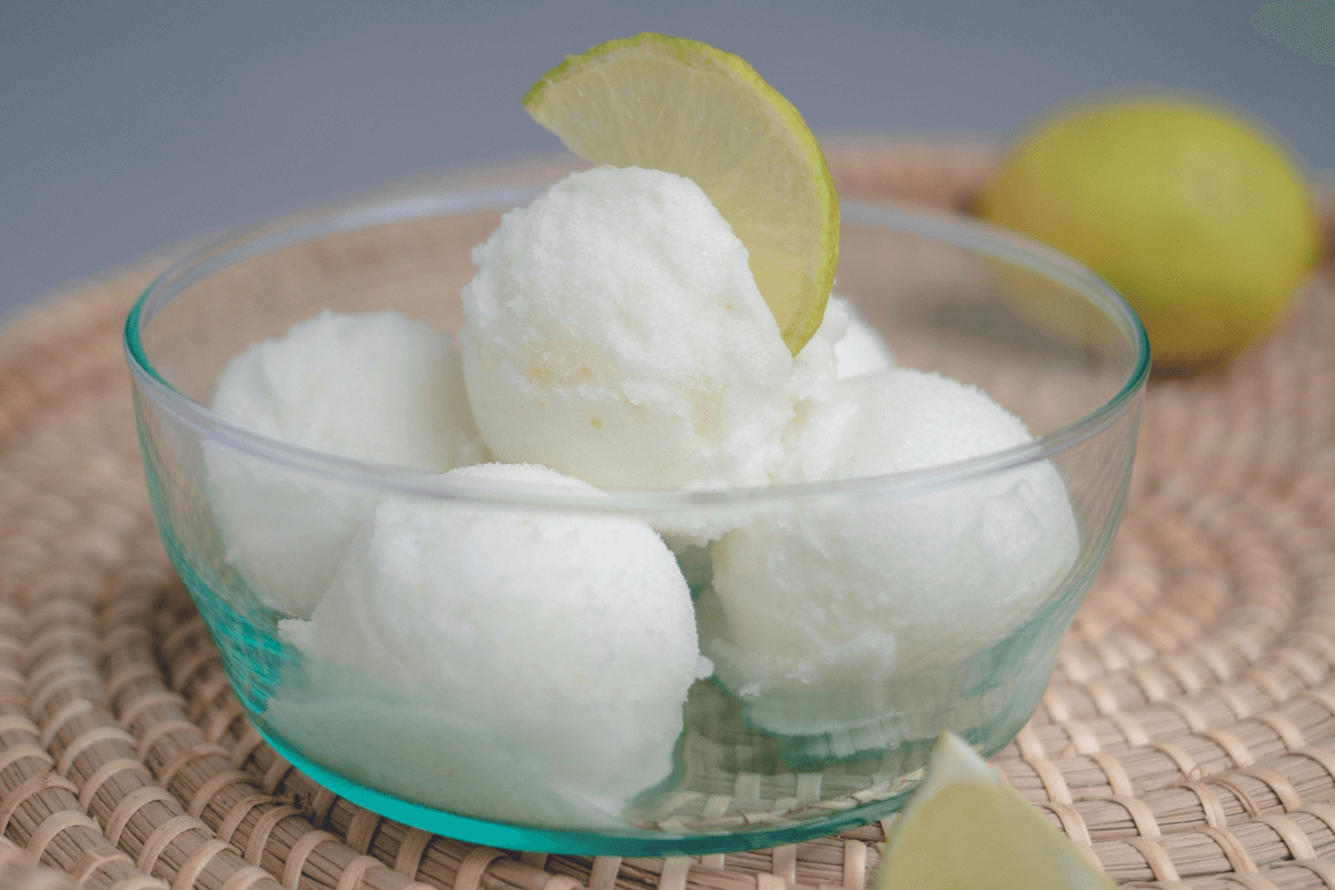 Schüssel mit Gin Tonic Sorbet, serviert mit einer Limettenscheibe. Hintergrund in sanften Farben.