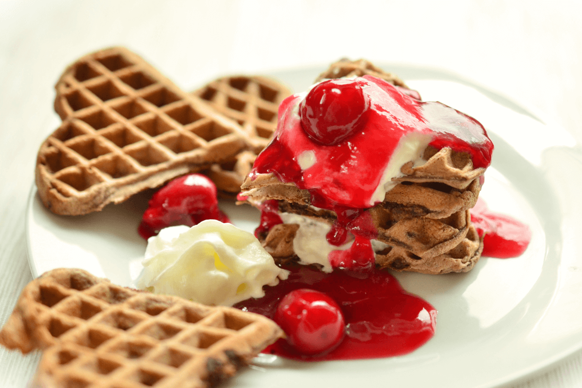 Herzwaffeln mit Amarettokirschen und Zimtsahne, dekoriert mit roter Kirschsoße und Sahne.
