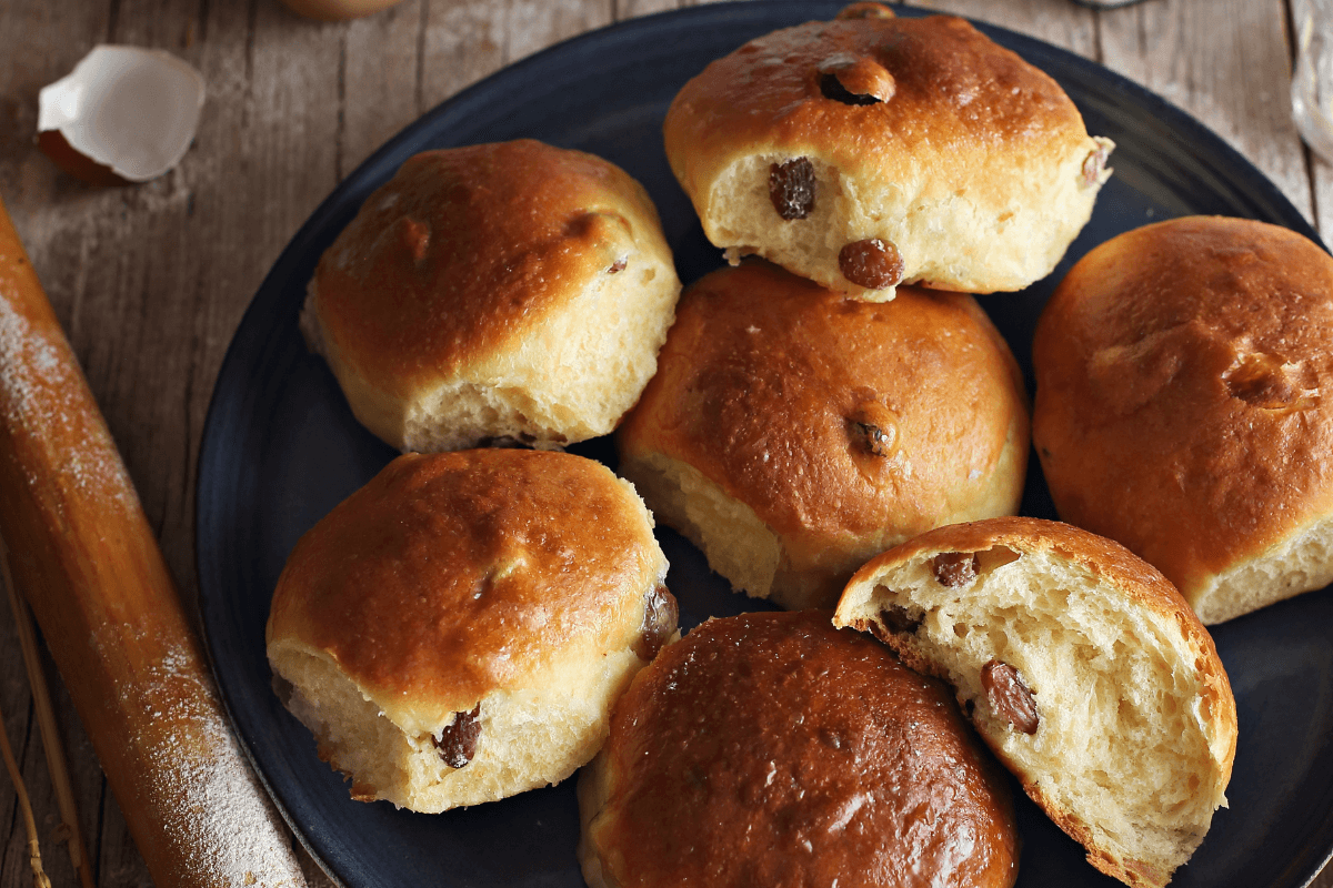 Frisch gebackene, goldbraune Brötchen mit Rosinen, auf einem blauen Teller angerichtet.