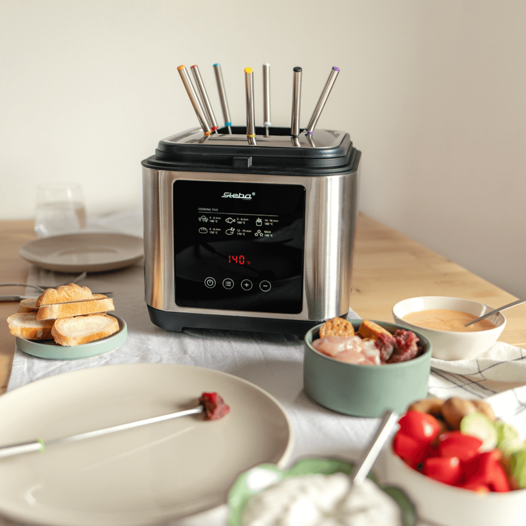 Steba DF150F Fritteuse mit digitalem Display, sechs Spießen, ideal für Fondue. Nebeneinander Teller mit Brot und Dips.