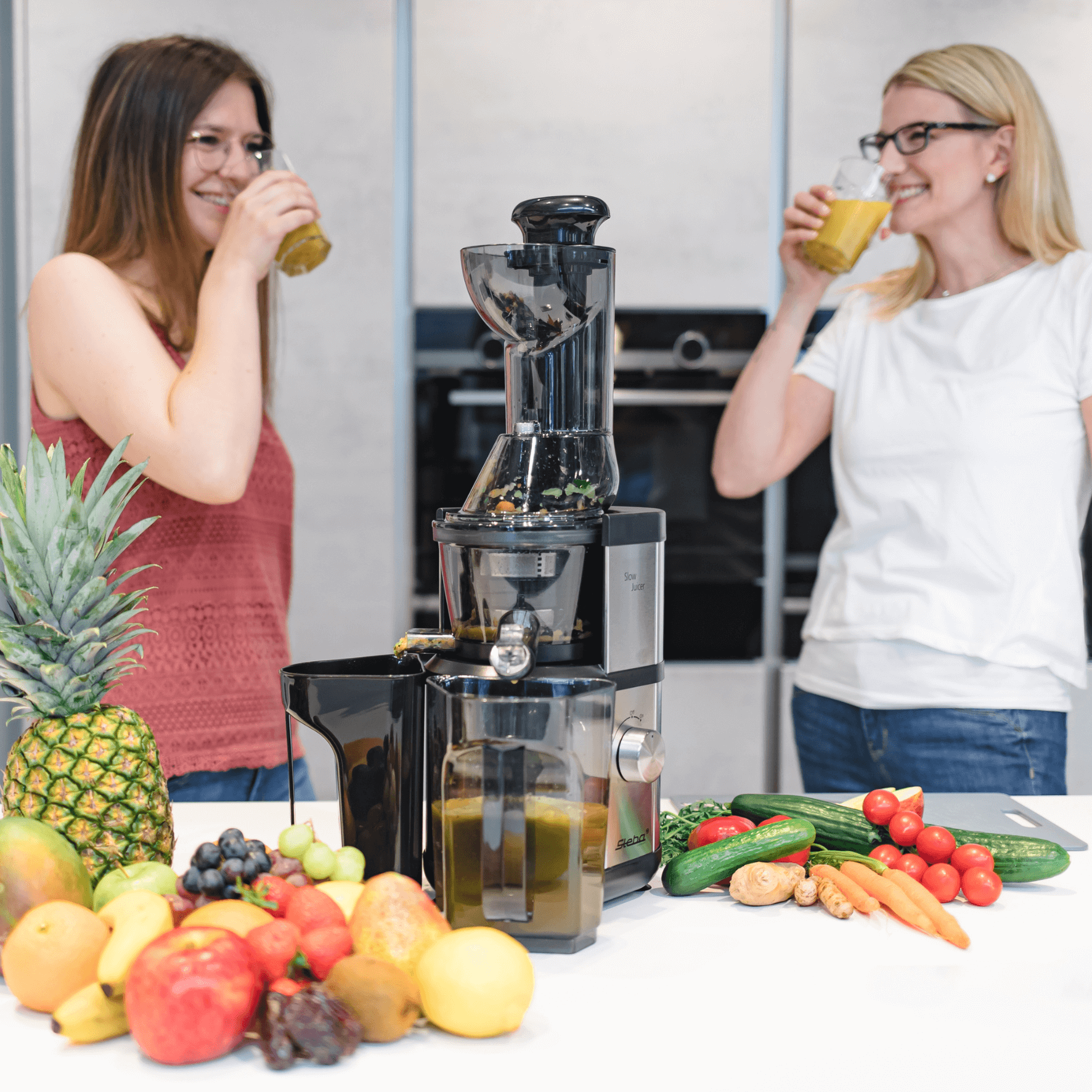 Slow Juicer von Steba mit frischem Obst und Gemüse, zwei Frauen genießen Saft. Praktische Entsafterfunktion und elegantes Design.