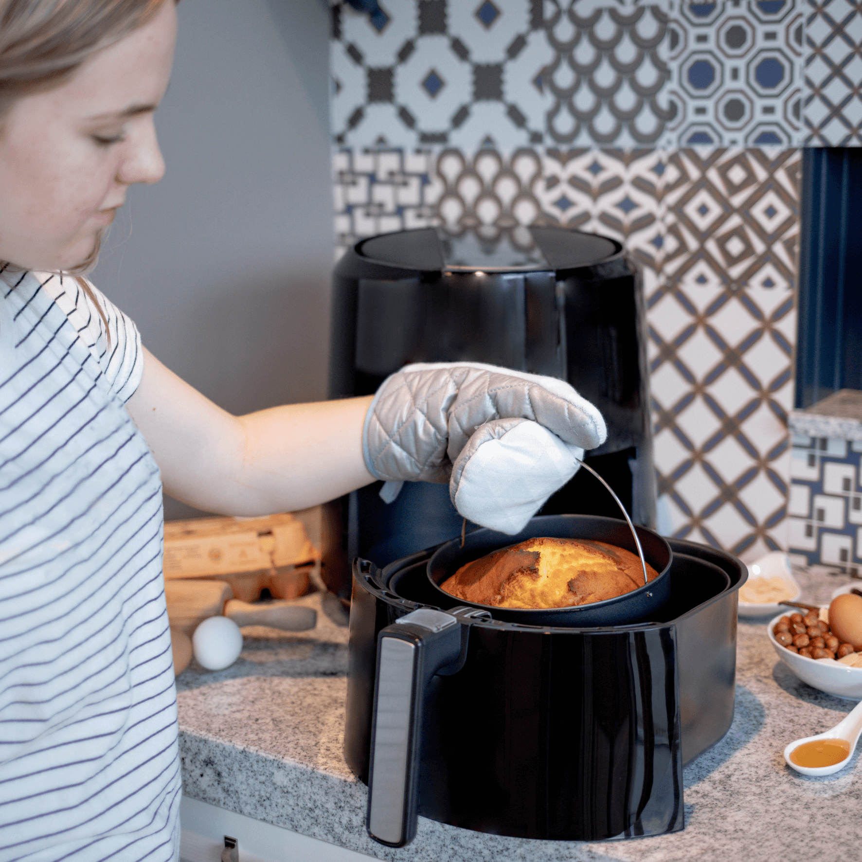 Eine Person mit einem Ofenhandschuh entnimmt eine Backform aus der Steba Heißluftfritteuse HF5000.