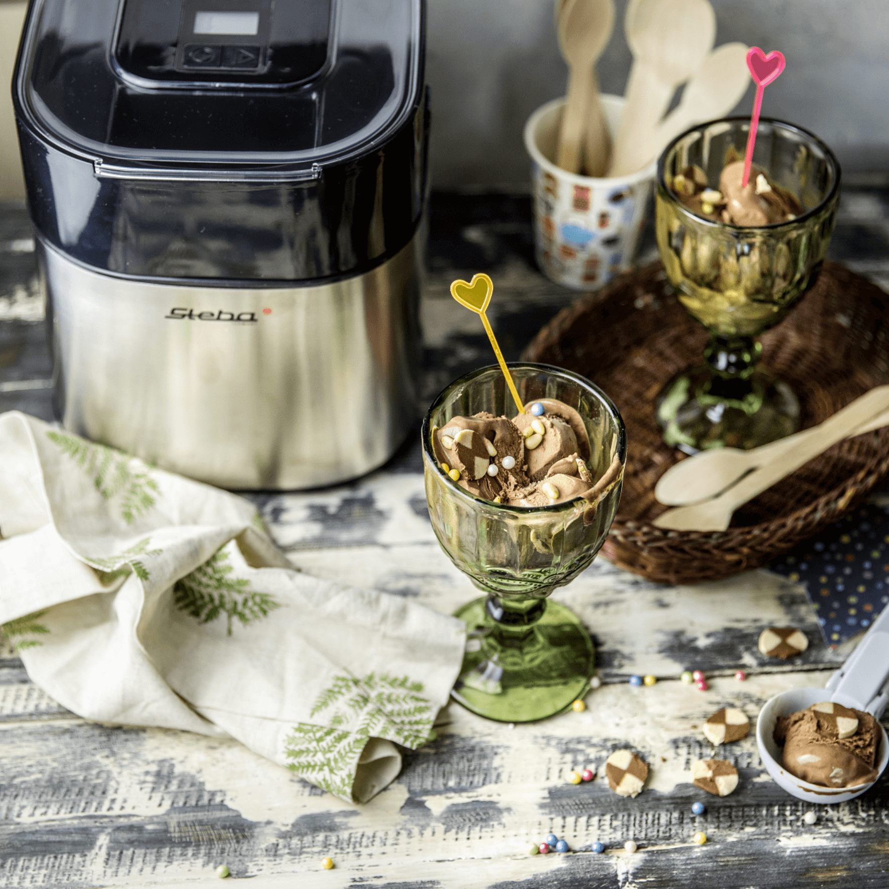 Steba Eismaschine IC30 in Edelstahloptik mit Schüssel, umgeben von Eisbechern, Löffeln und einer Serviette.