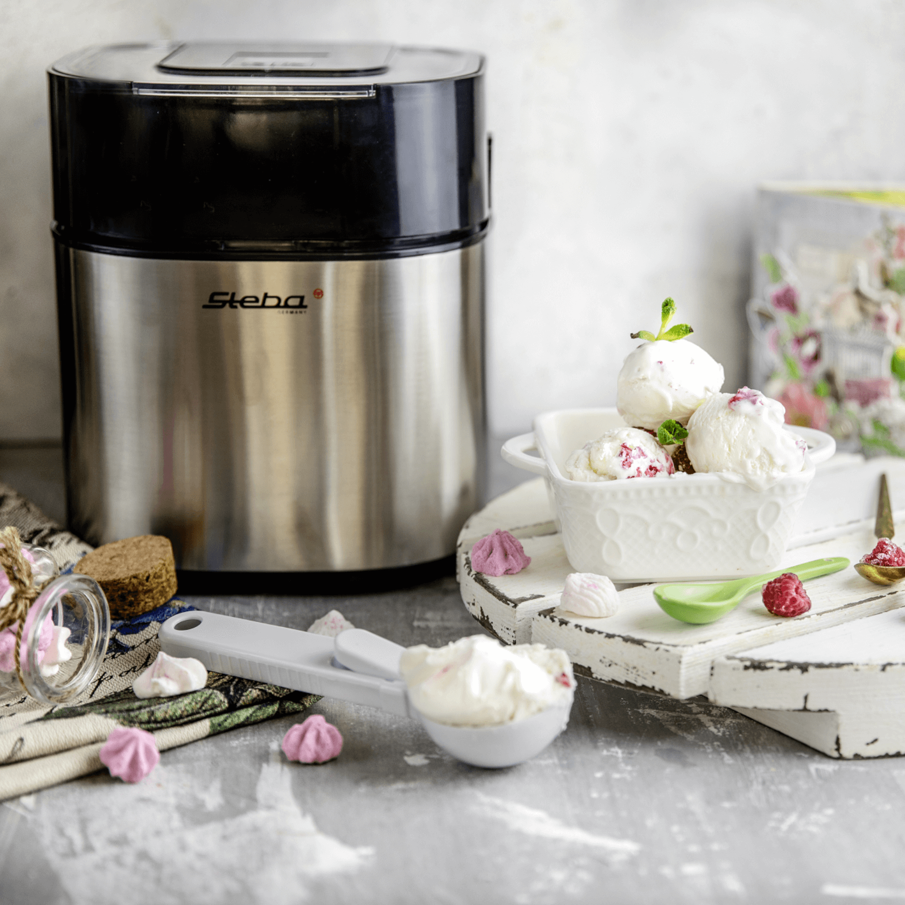 Steba Eismaschine mit Edelstahl-Gehäuse, daneben eine Schüssel mit Eiscreme, Löffel und süßen Dekorationen.