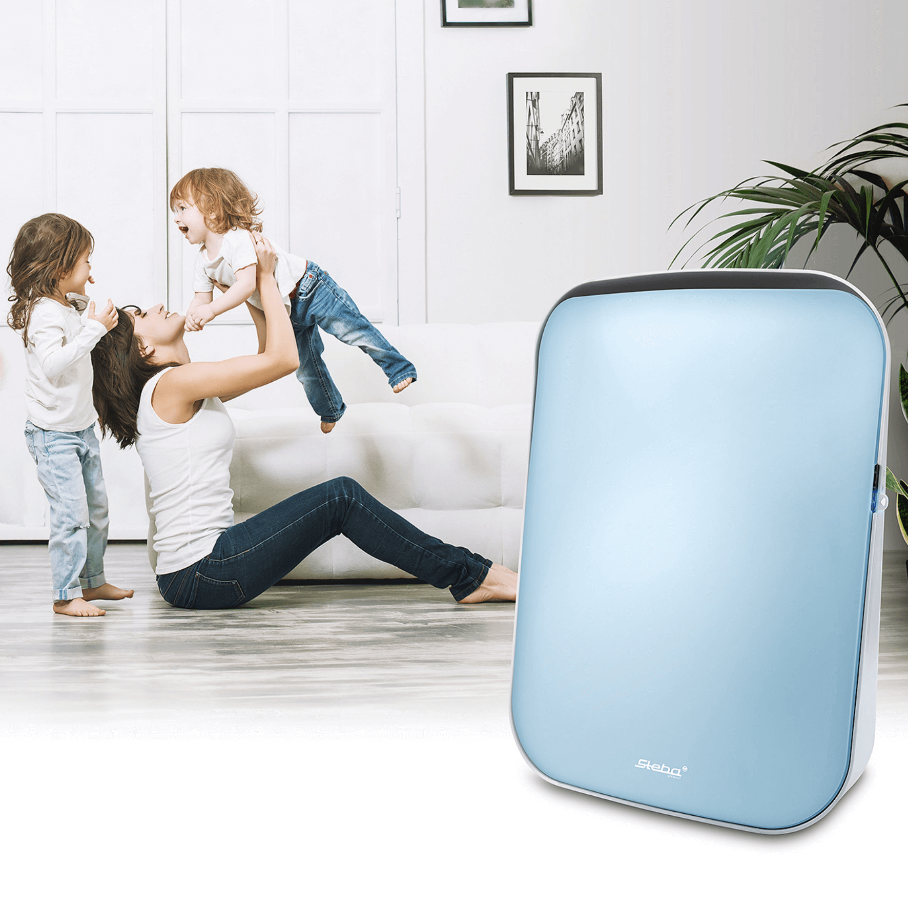 Luftreiniger Steba LR9 in sanftem Blau, im Vordergrund, während eine Mutter mit zwei Kindern im Hintergrund spielt.