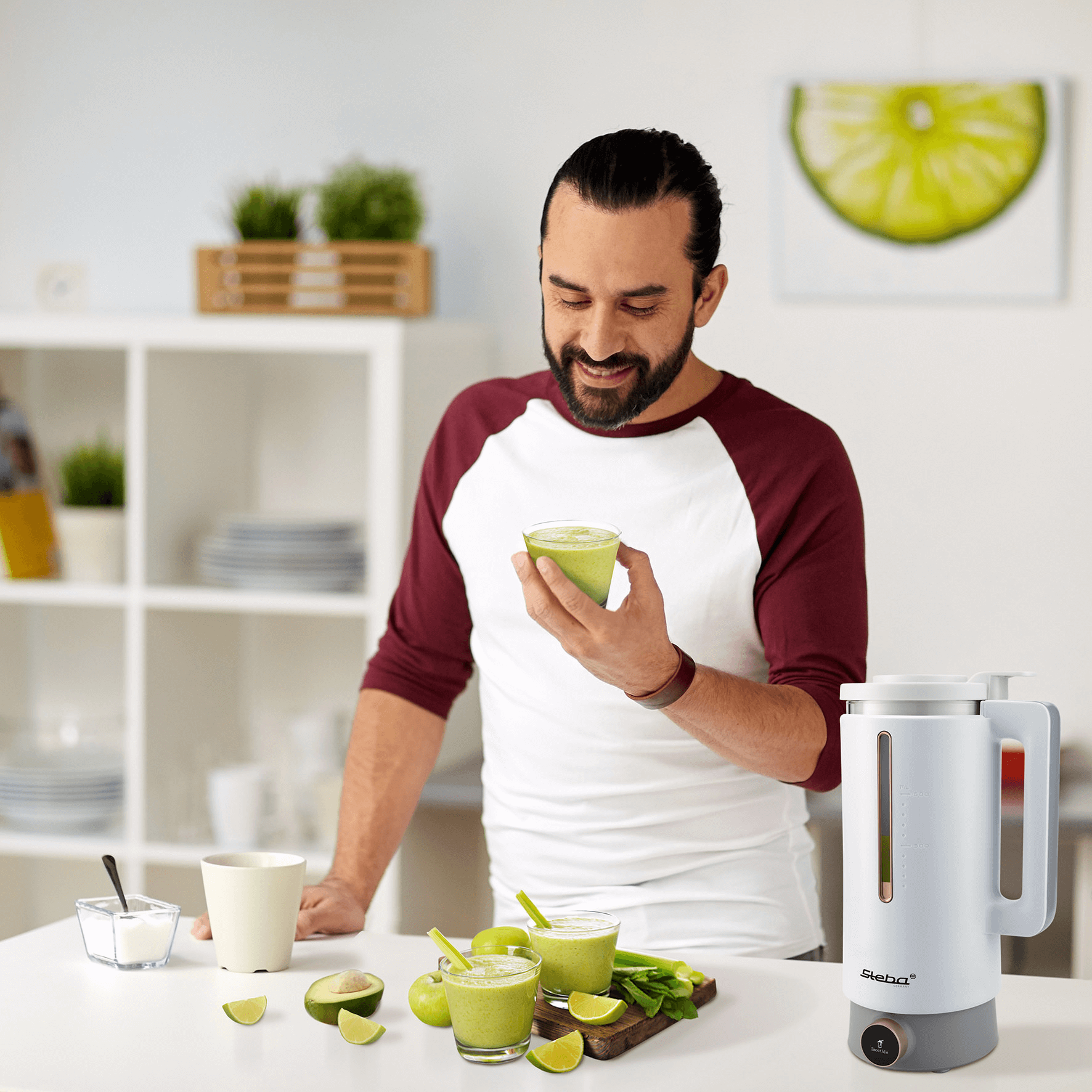Der Steba VDM2 Vegan Drink Maker steht auf einem Tisch. Ein Mann hält ein Glas mit grünem Smoothie, umgeben von weiteren Getränken und Zutaten.