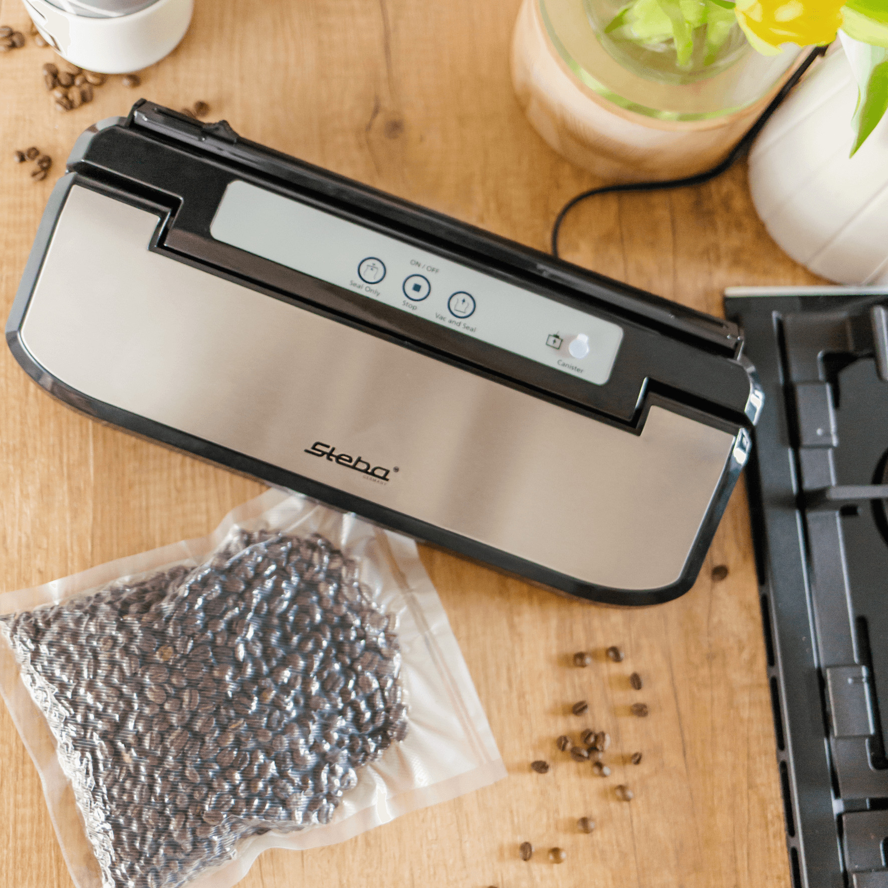 Vakuumierer von Steba mit Edelstahl-Oberfläche und Bedienelementen, neben vakuumierten Kaffeebohnen auf Holzunterlage.