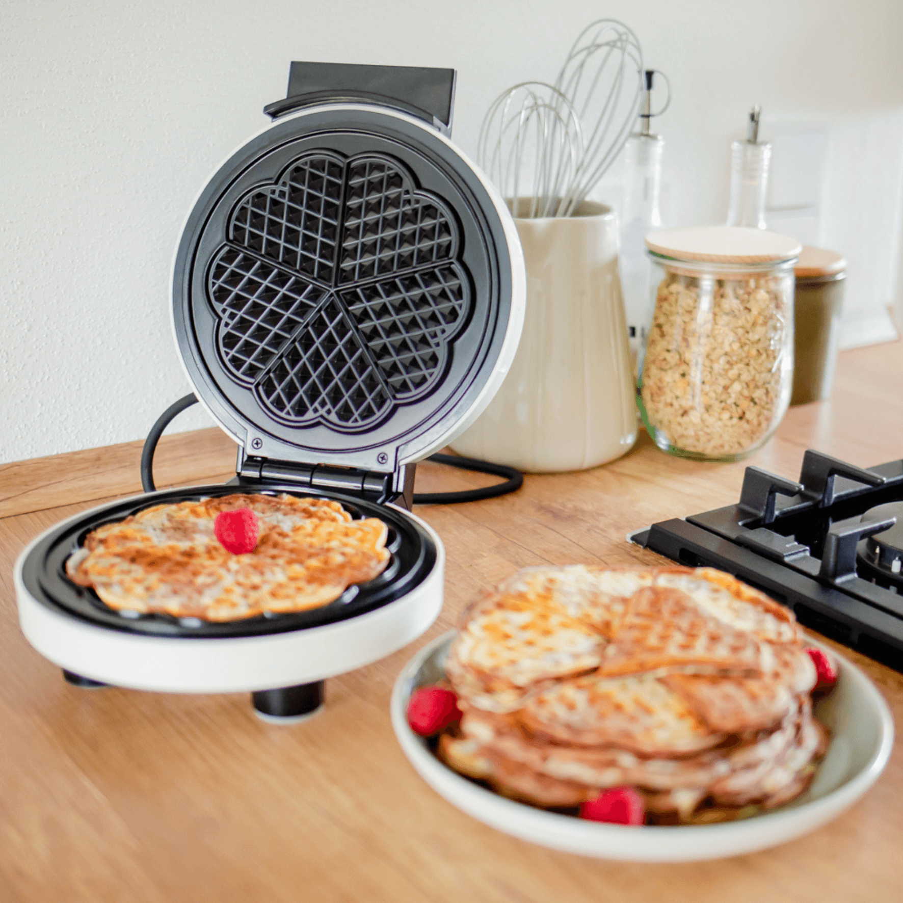 Waffeleisen von Steba mit runder Backfläche und dekorativem Muster. Darin befinden sich frisch gebackene Waffeln, serviert mit Himbeeren.
