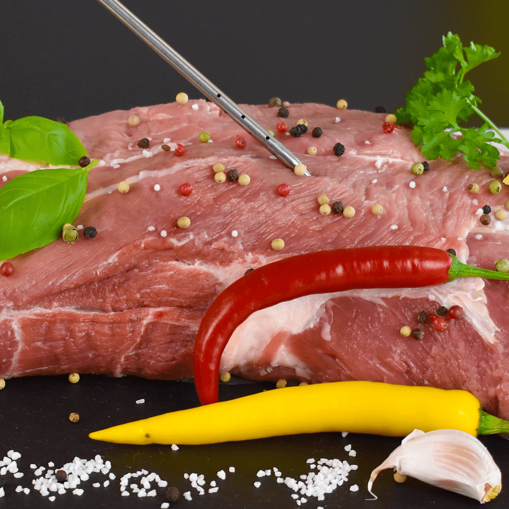 Frisches Fleisch mit Gewürzen, Paprika und Kräutern, daneben eine Marinadenspritze von Steba.