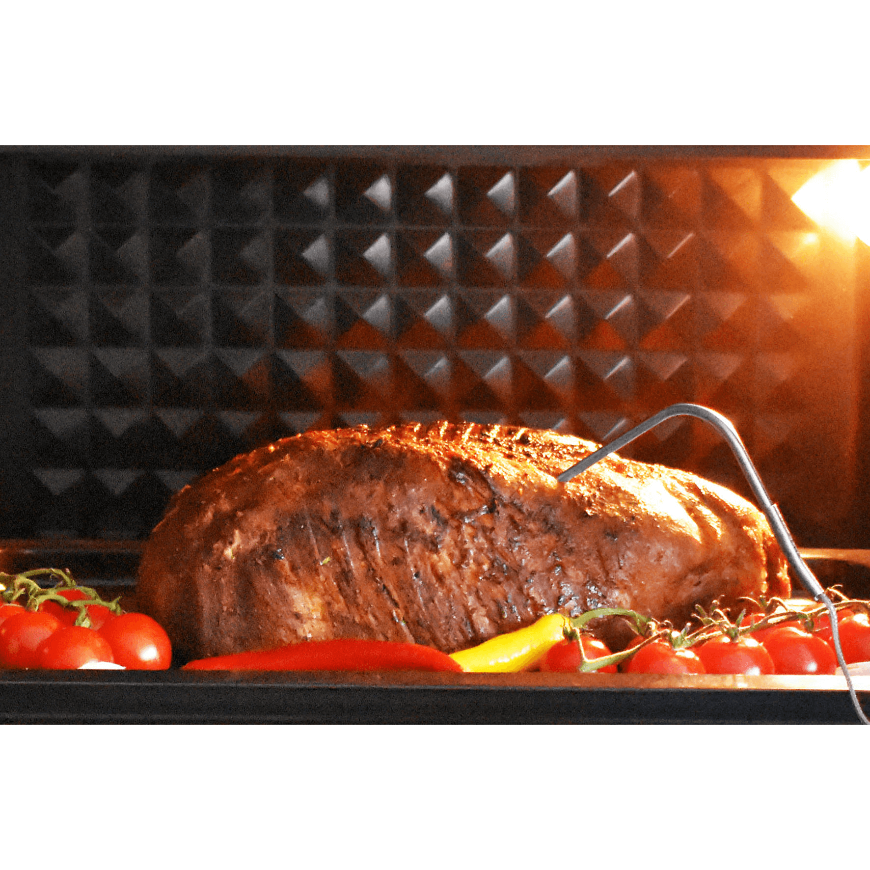 Saftiger Braten im Ofen, umgeben von frischen Tomaten und Paprika, mit einem Fleischthermometer zur Temperaturkontrolle.