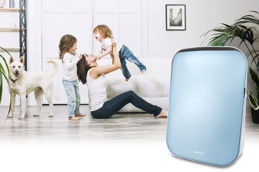 Luftreiniger in modernem Design steht neben einer Familie mit zwei Kindern und einem Hund in einem hellen Wohnzimmer.