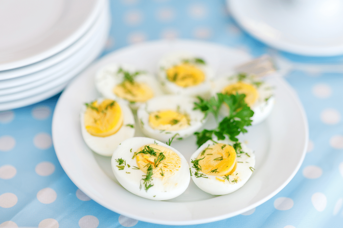 Ein Teller mit halbierten, gekochten Eiern, dekoriert mit frischen Kräutern, auf einem blauen Tisch mit weißen Punkten.