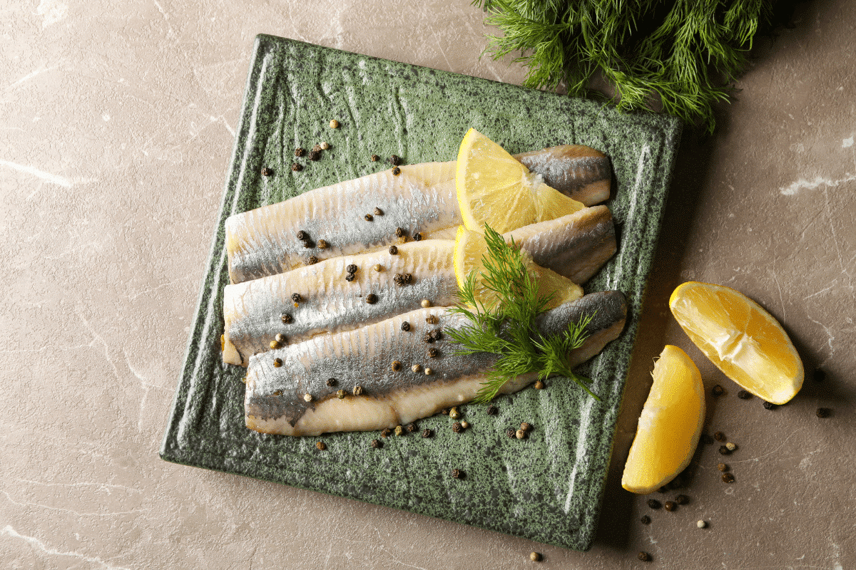 Rotbarschfilets mit Zitronenscheiben und Dill auf einem grünen Teller, garniert mit Pfefferkörnern.