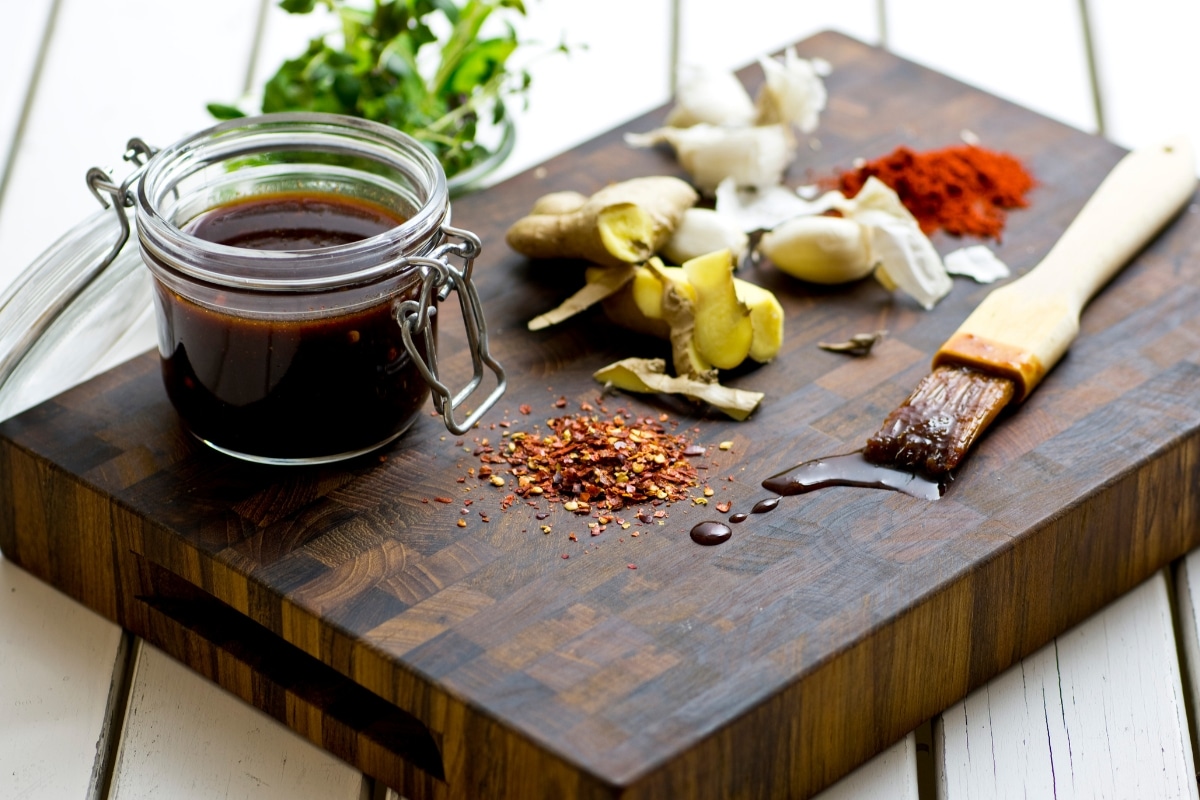 Glas mit Steba Teriyaki-Marinade, umgeben von Gewürzen, Ingwer und Knoblauch auf einem Holzbrett.
