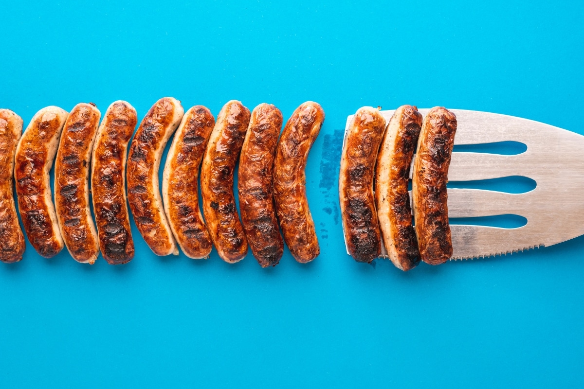Bratwürste Nürnberger Art auf einem großen Spatel, vor einem blauen Hintergrund, gleichmäßig angeordnet.