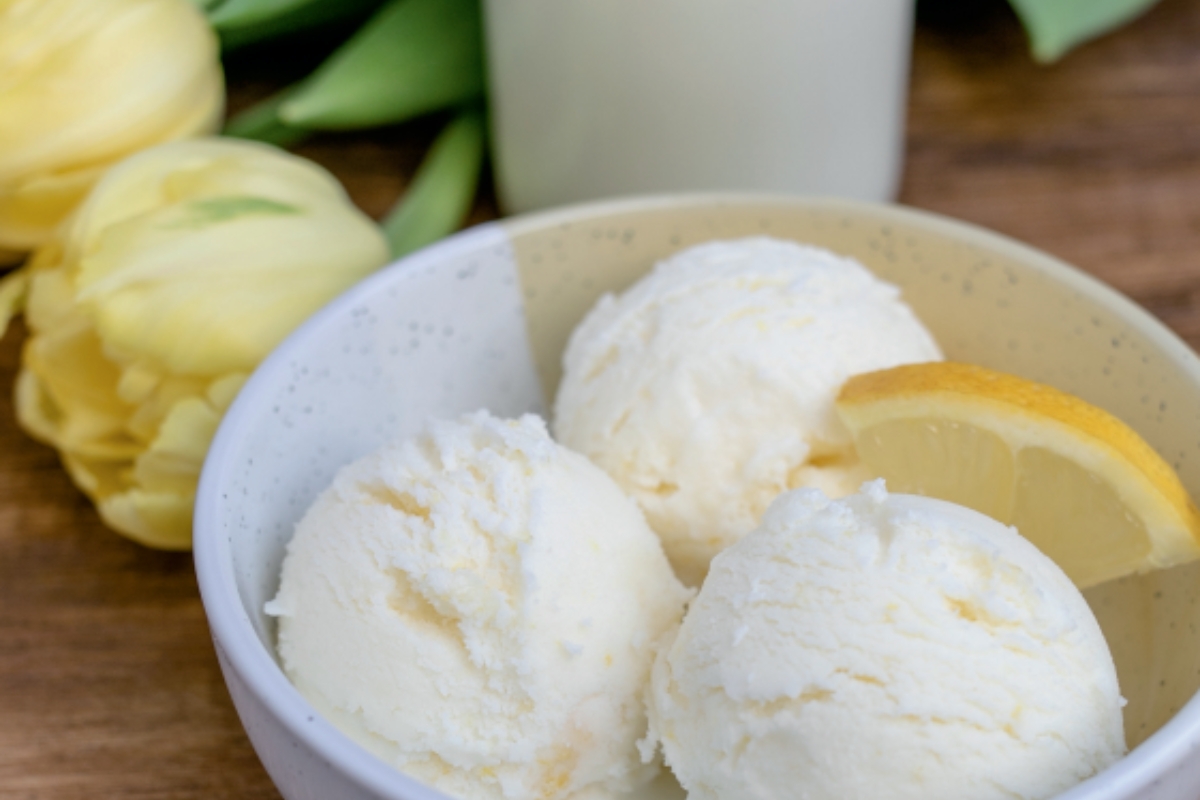 Zitrone-Buttermilch Eis in einer Schüssel, garniert mit einer Zitronenscheibe und umgeben von gelben Tulpen.