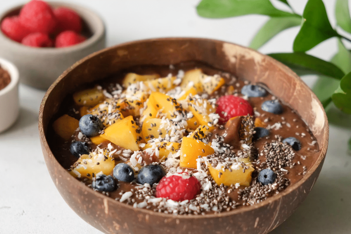 Schoko-Bananen Nicecream Bowl in einer Kokosnusschale, dekoriert mit Früchten, Chiasamen und Kokosraspeln.