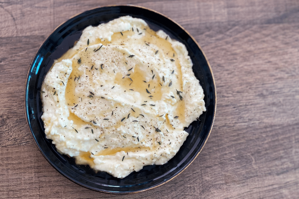 Cremiger Camembert-Dip in schwarzem Teller, mit Olivenöl und Thymian gewürzt, auf Holzuntergrund.