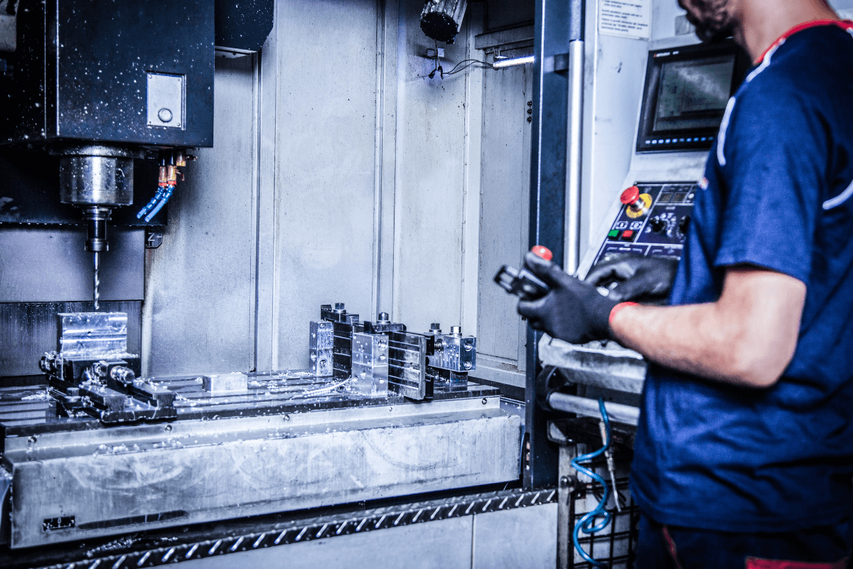 CNC-Fräse in einer Werkstatt, der Bediener überwacht den Prozess. Metallteile werden bearbeitet, Späne sind sichtbar.
