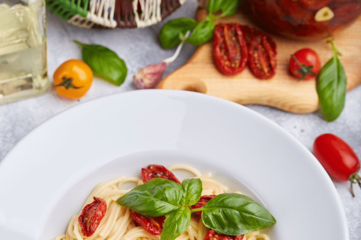 Spaghetti mit getrockneten Tomaten, garniert mit frischem Basilikum, serviert auf einem weißen Teller.