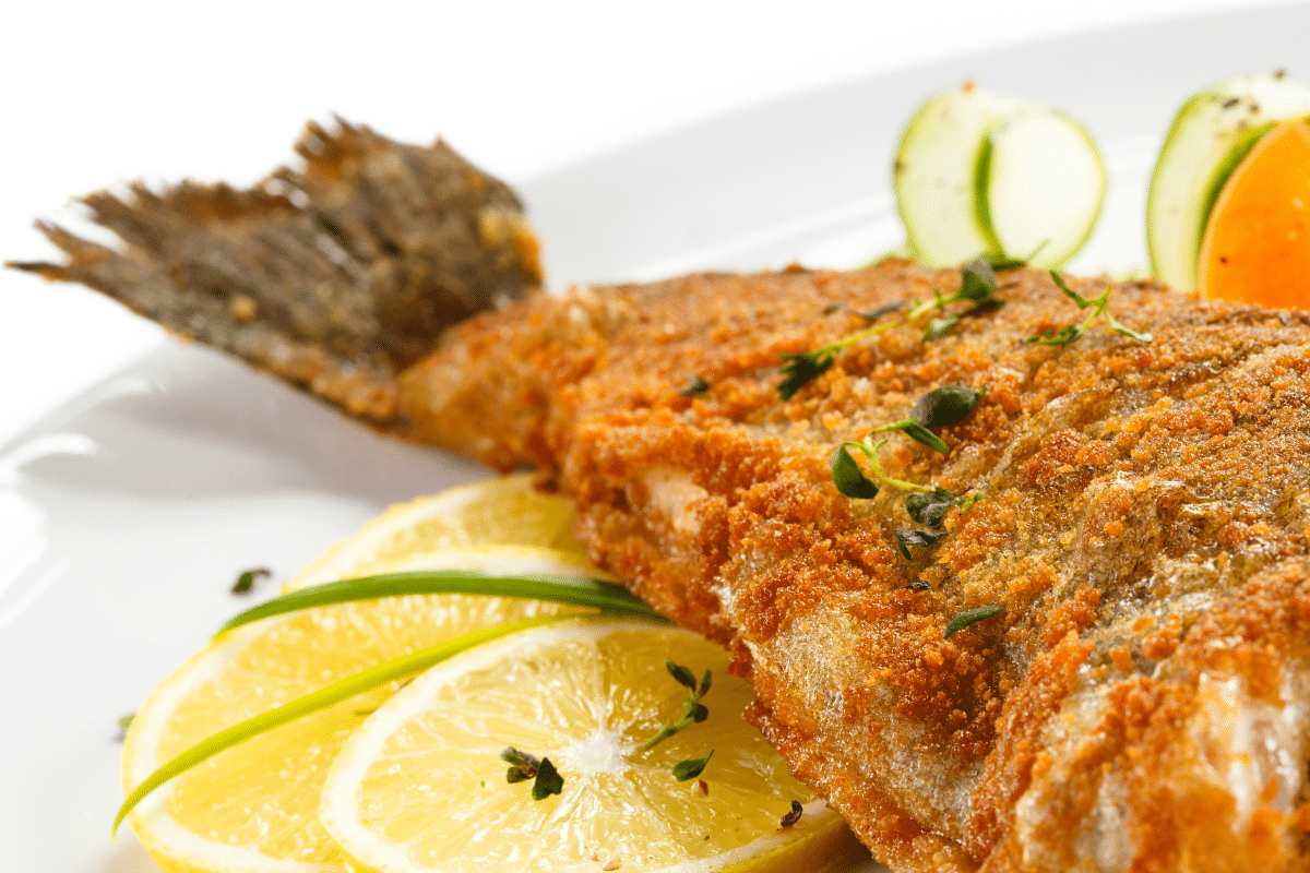 Gebackener Karpfen auf einem weißen Teller, serviert mit Zitronenscheiben und frischen Kräutern.