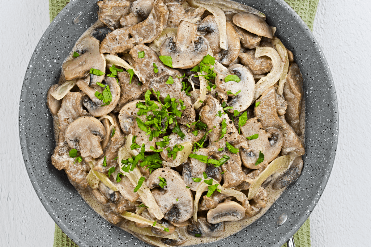 Eine Pfanne mit Zürcher Geschnetzeltem, bestehend aus zarten Fleischstreifen, Champignons und Zwiebeln in einer cremigen Sauce, garniert mit frischem Schnittlauch.