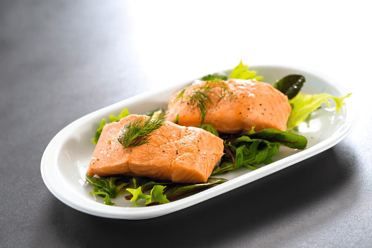 Sous-Vide gegartes Lachsfilet auf einem Bett aus frischem Salat, garniert mit Dill und Pfeffer.