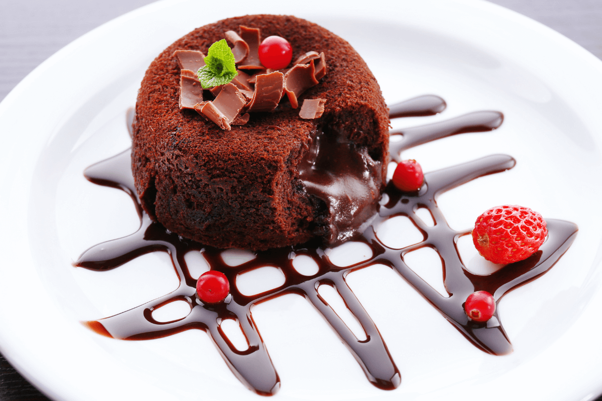 Schokoladen-Lava-Kuchen auf einem weißen Teller, dekoriert mit Schokoladenraspeln, frischen Erdbeeren und einer Schokoladensauce.