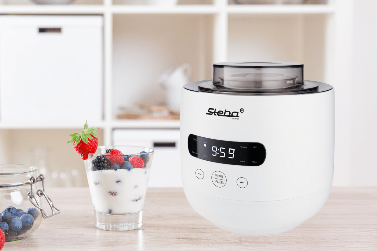 Steba Joghurt-Maker JM 4 FERMENT in Weiß mit digitalem Display und Tasten. Neben einem Glas mit Joghurt und Beeren.