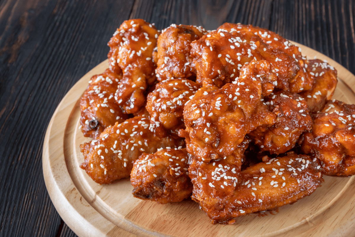 Knusprige Chicken Tenders, glasiert mit einer würzigen Sauce und bestreut mit Sesam, auf einem Holzbrett präsentiert.