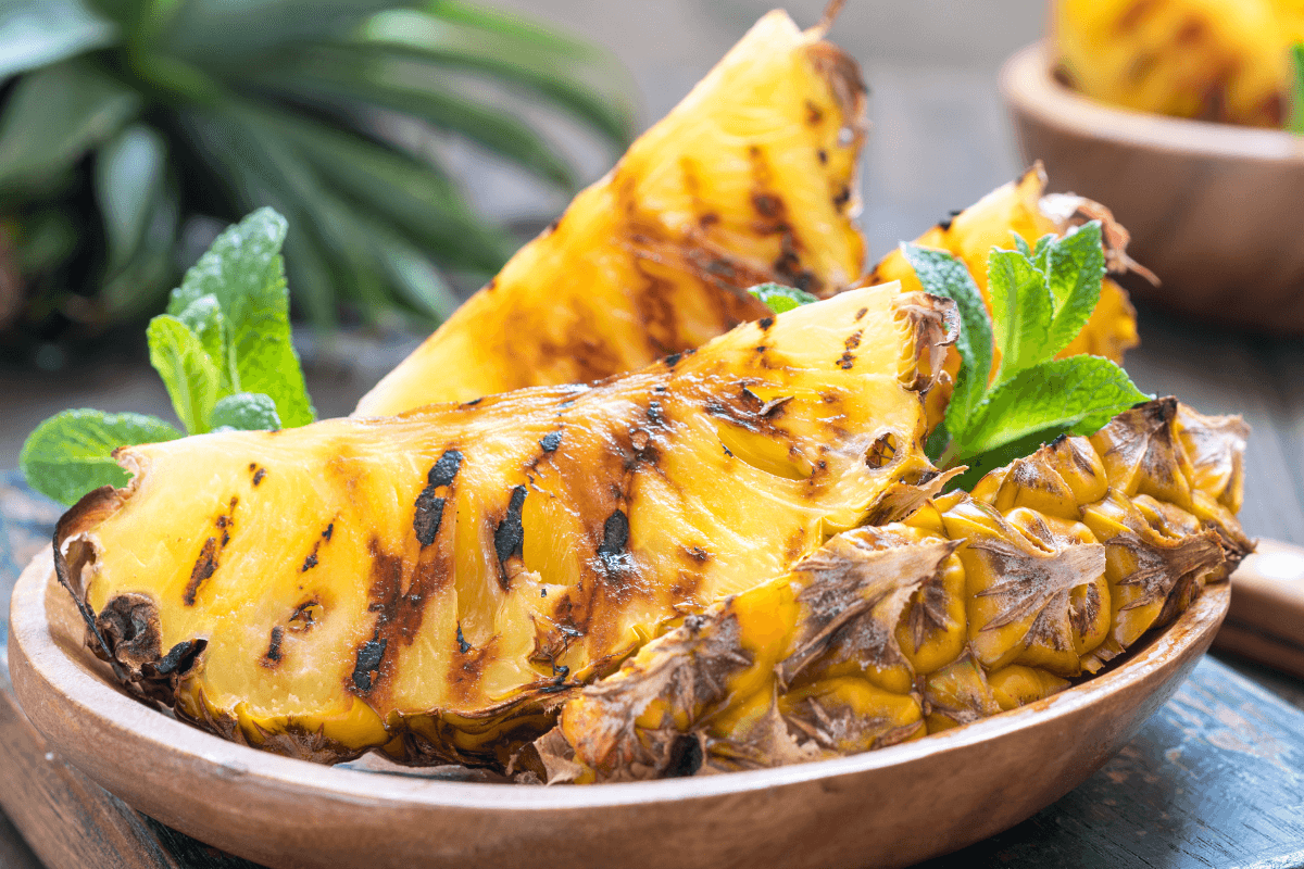 Gegrillte Ananasstücke in einer Holzschüssel, garniert mit frischer Minze. Lecker und dekorativ angerichtet.