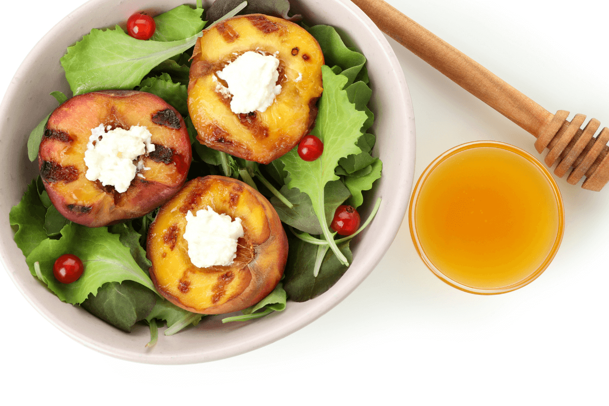 Gegrillte Pfirsiche mit Ziegenkäse auf einem Bett aus frischem Salat, daneben ein Glas Honig-Balsamico-Glasur.