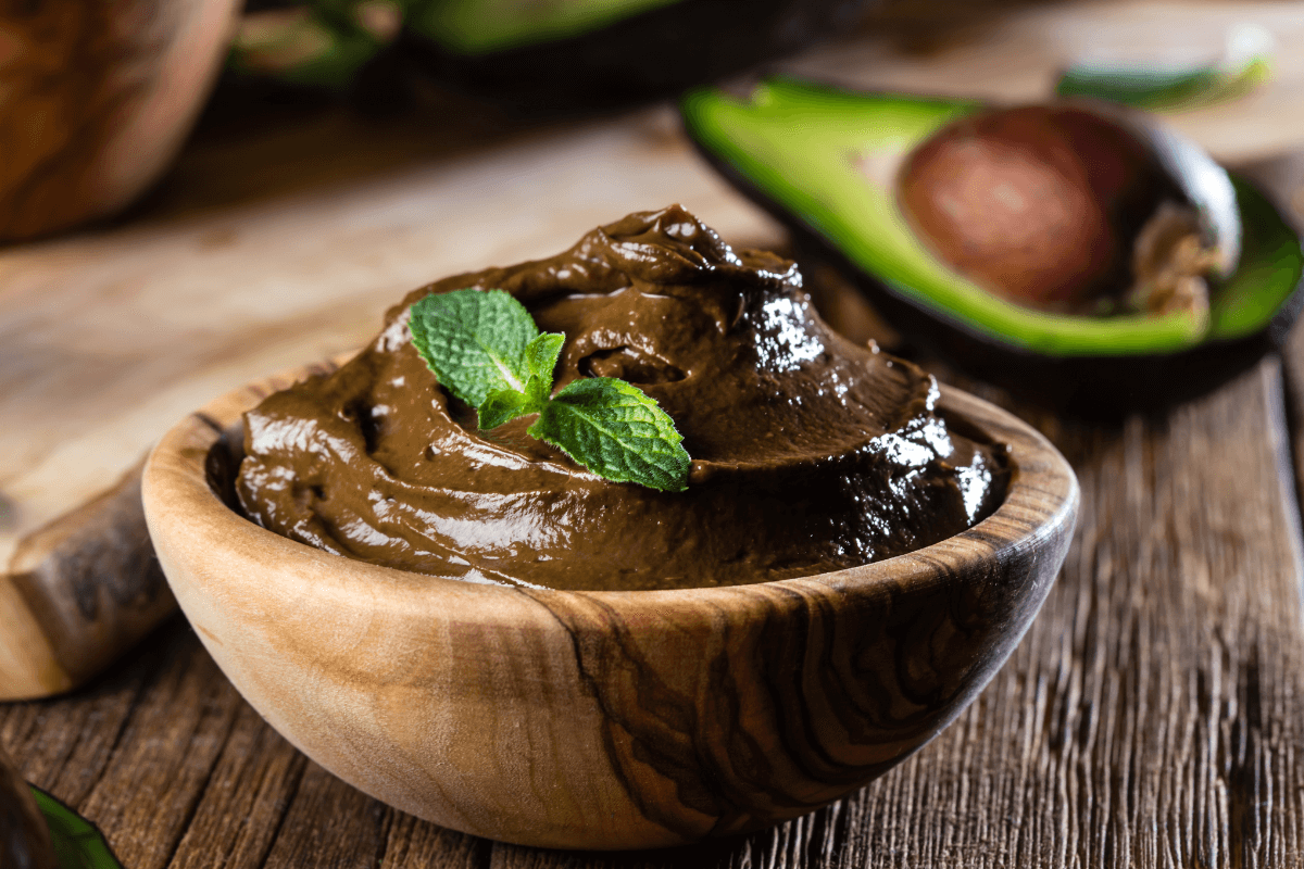 Avocado-Schokoladen-Mousse in einer Holzschale, garniert mit frischer Minze, auf einem rustikalen Holztisch.