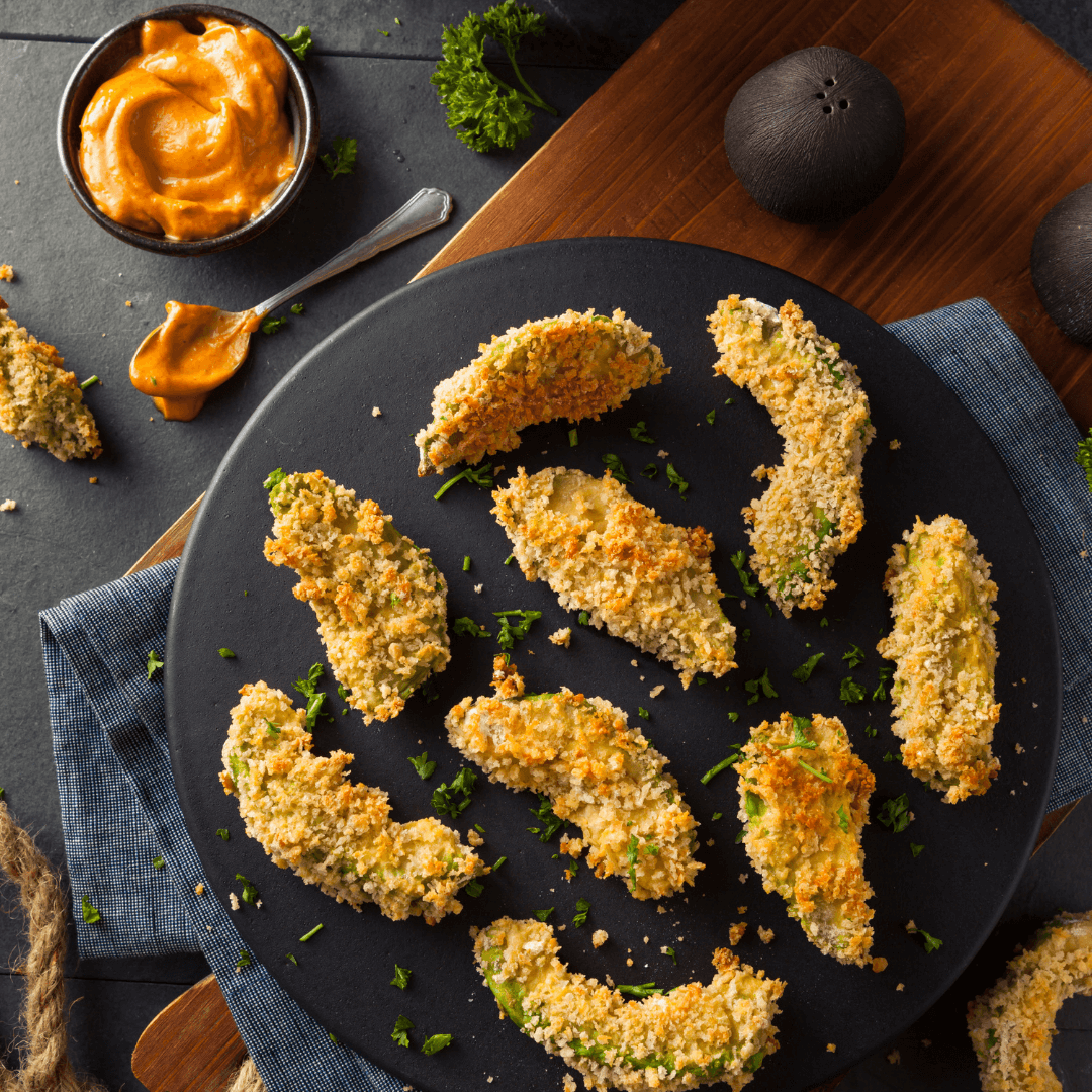 Crunchy Avocado Pommes auf einem schwarzen Teller, garniert mit Petersilie und einer Schale mit cremigem Dip.