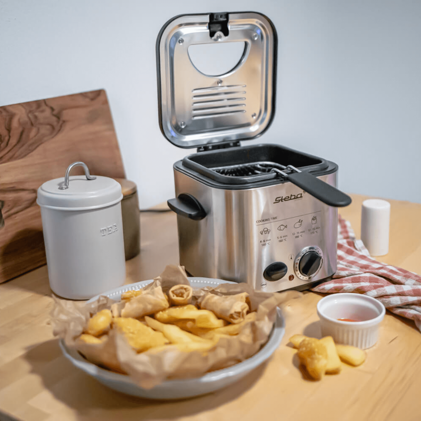 Steba DF95 Fritteuse aus Edelstahl mit Frittierkorb, daneben ein Teller mit frittierten Snacks und Dipsauce.