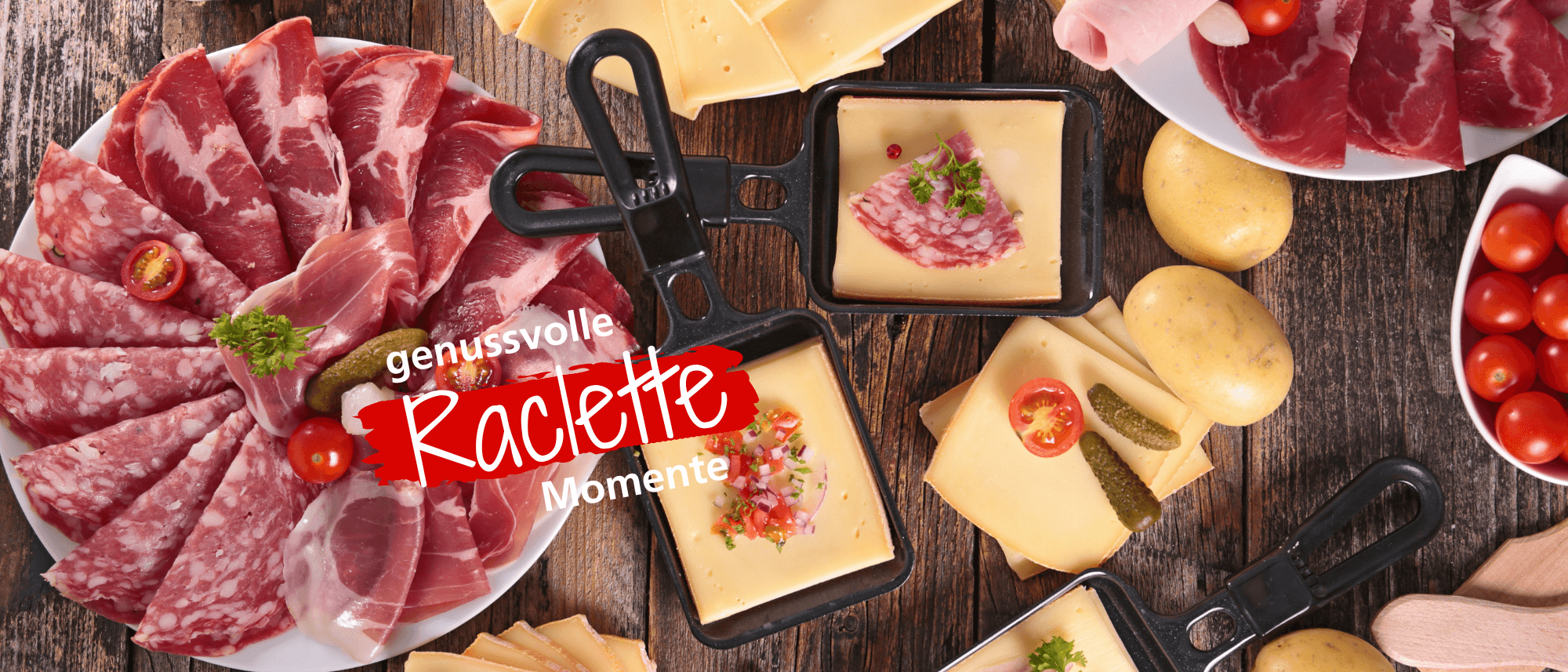 Vielfalt an Raclette-Zutaten: verschiedene Wurstsorten, Käse, Kartoffeln, Tomaten und Gewürzgurken auf einem rustikalen Tisch.