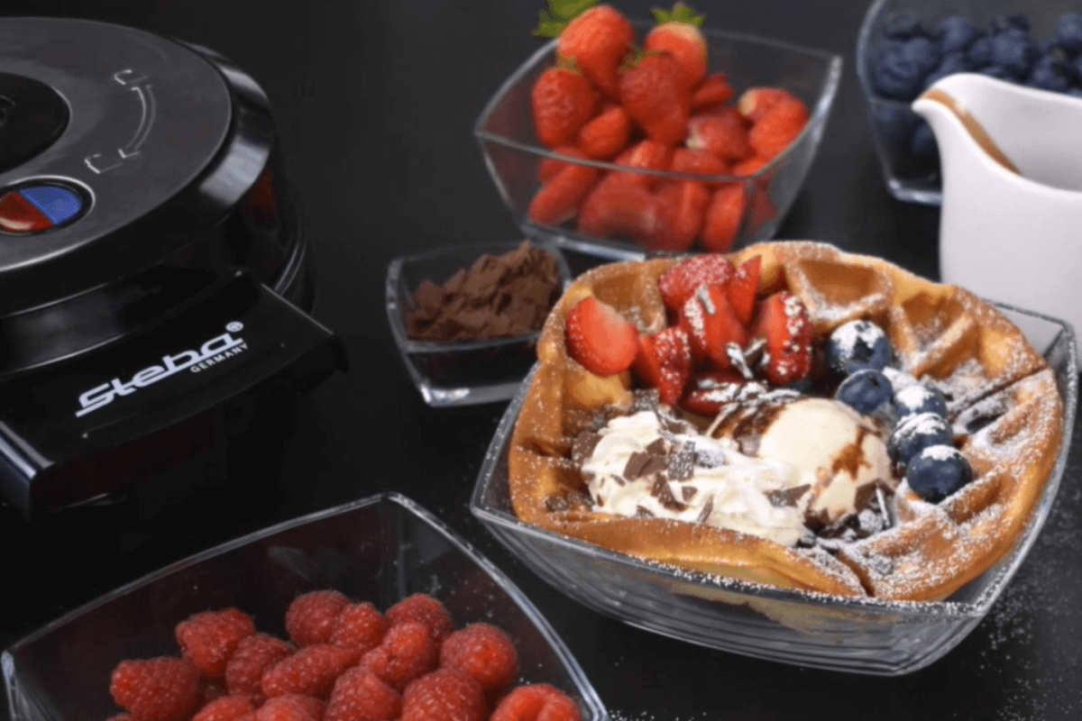 Steba Waffeleisen mit frisch zubereiteten belgischen Waffeln, garniert mit Früchten, Schokolade und Sahne.