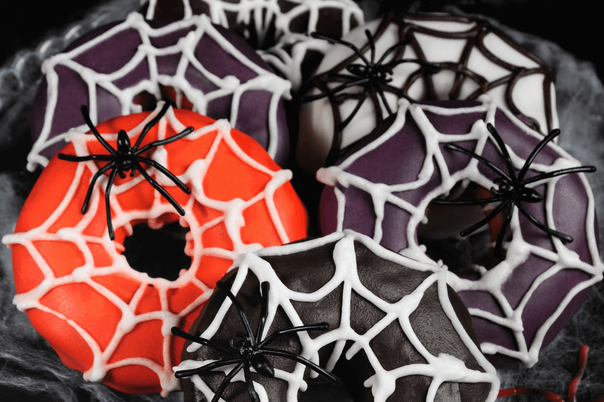 Bunte Halloween Donuts in Orange, Lila und Schwarz, dekoriert mit Spinnen und Spinnennetz-Muster aus Zuckerguss.