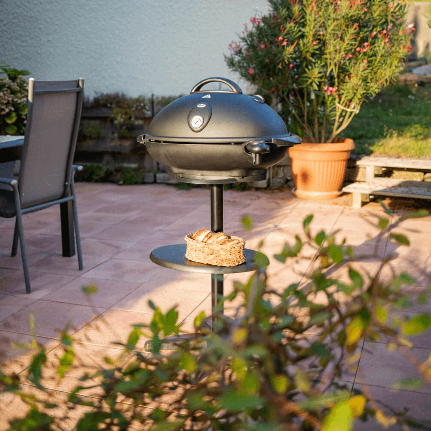 Schwarzer VG350 BBQ-Grill von Steba auf einem Ständer, umgeben von Pflanzen und einem Tisch im Garten.