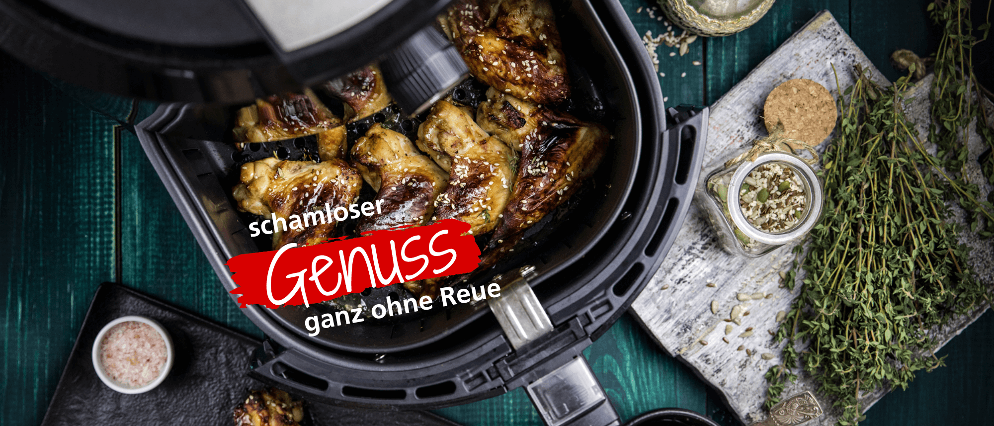 Airfryer von Steba mit knusprig gebratenen Hähnchenteilen. Umgeben von frischen Kräutern und Gewürzen auf einem Holzuntergrund.