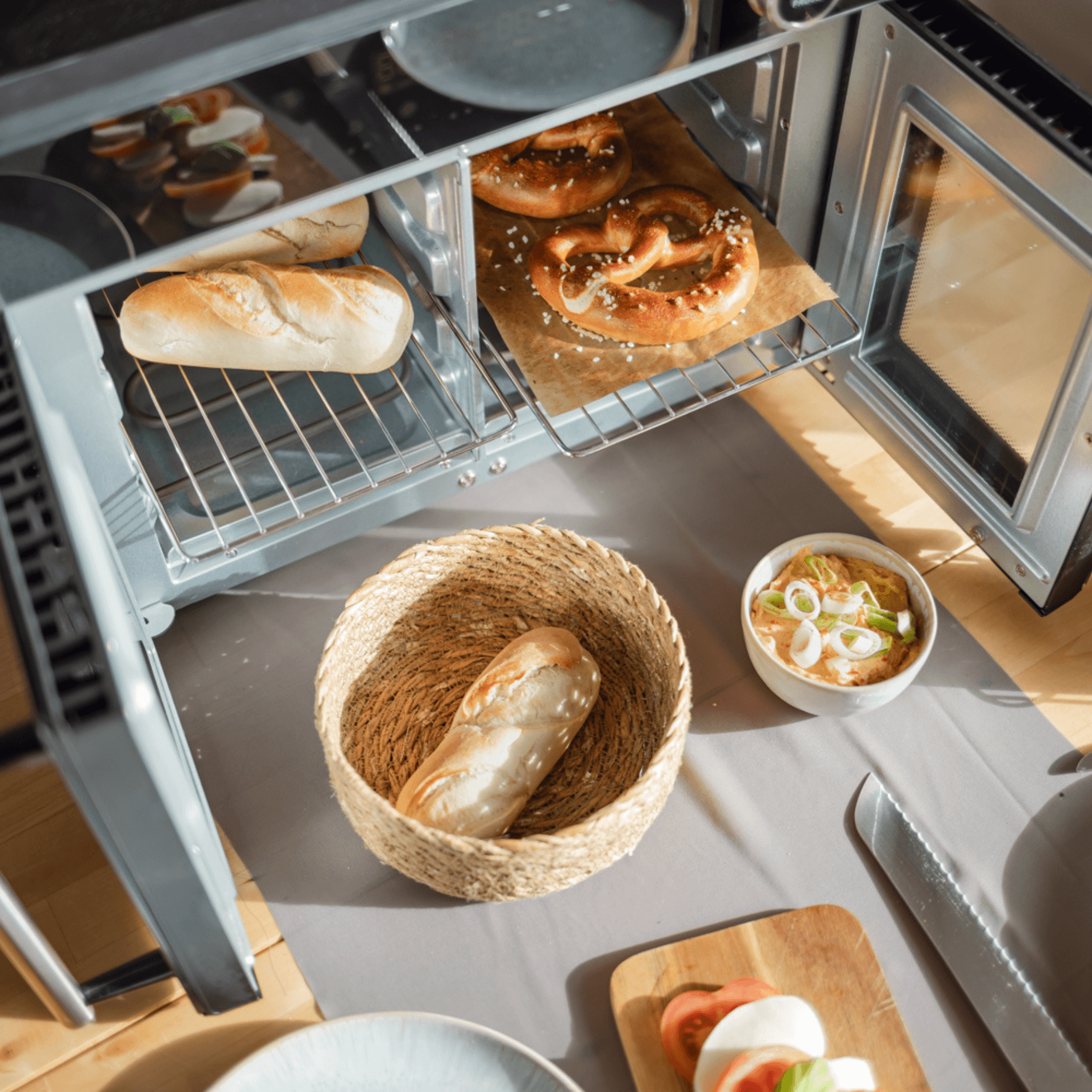 Airfryofen von Steba mit frischem Brot und Brezeln im Innenraum, umgeben von einer dekorativen Schüssel und Zutaten.