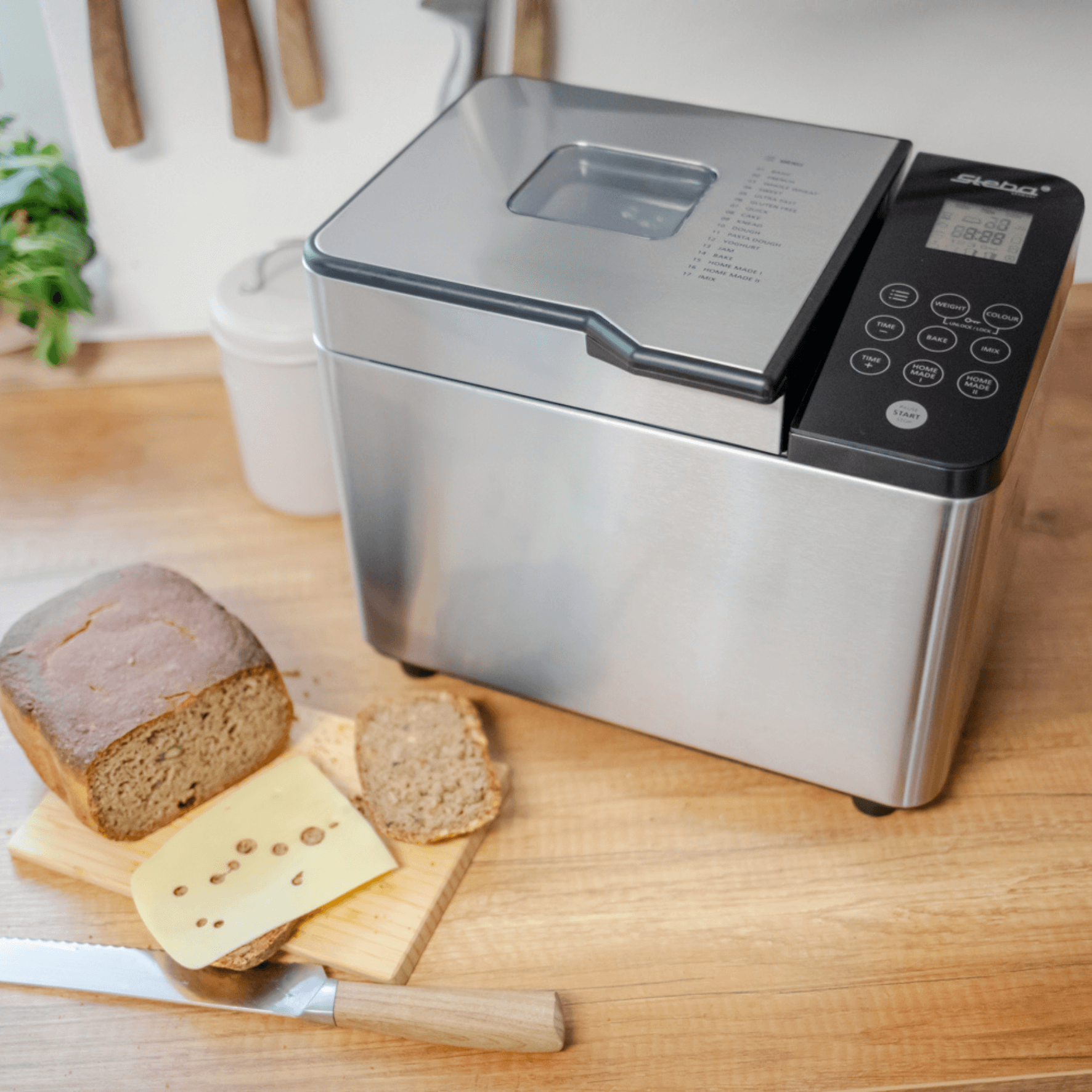 Brotbackautomat von Steba mit digitalem Display, neben frisch gebackenem Brot und Käse auf einem Holzbrett.