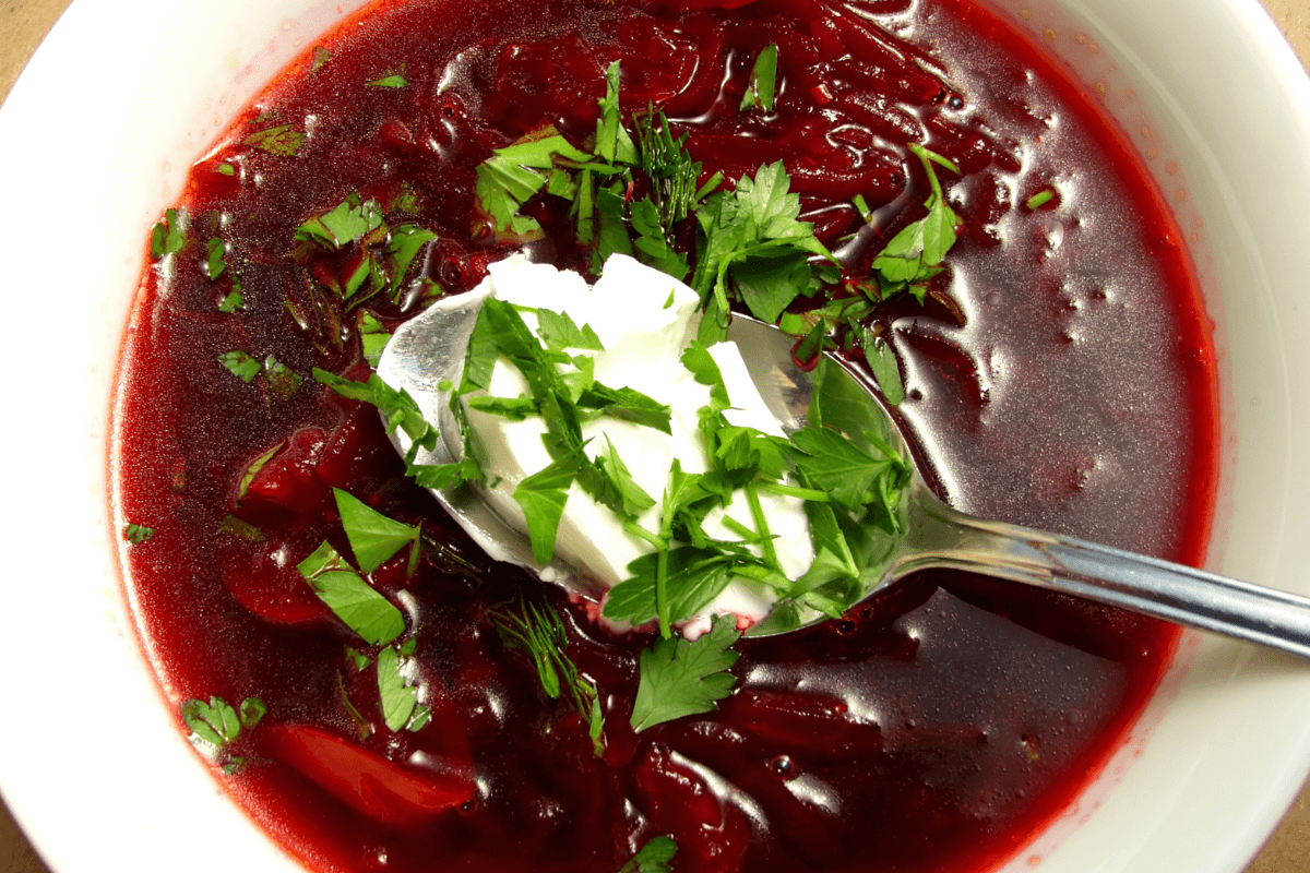 Schüssel mit Borschtsch, garniert mit frischem Dill und Petersilie sowie einem Löffel saurer Sahne.