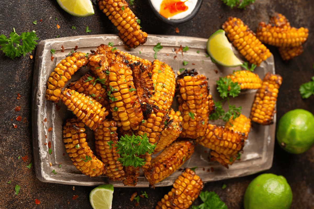 Gegrillte Corn Ribs mit BBQ-Glasur, garniert mit frischem Koriander und Limettenscheiben, serviert auf einer Platten.